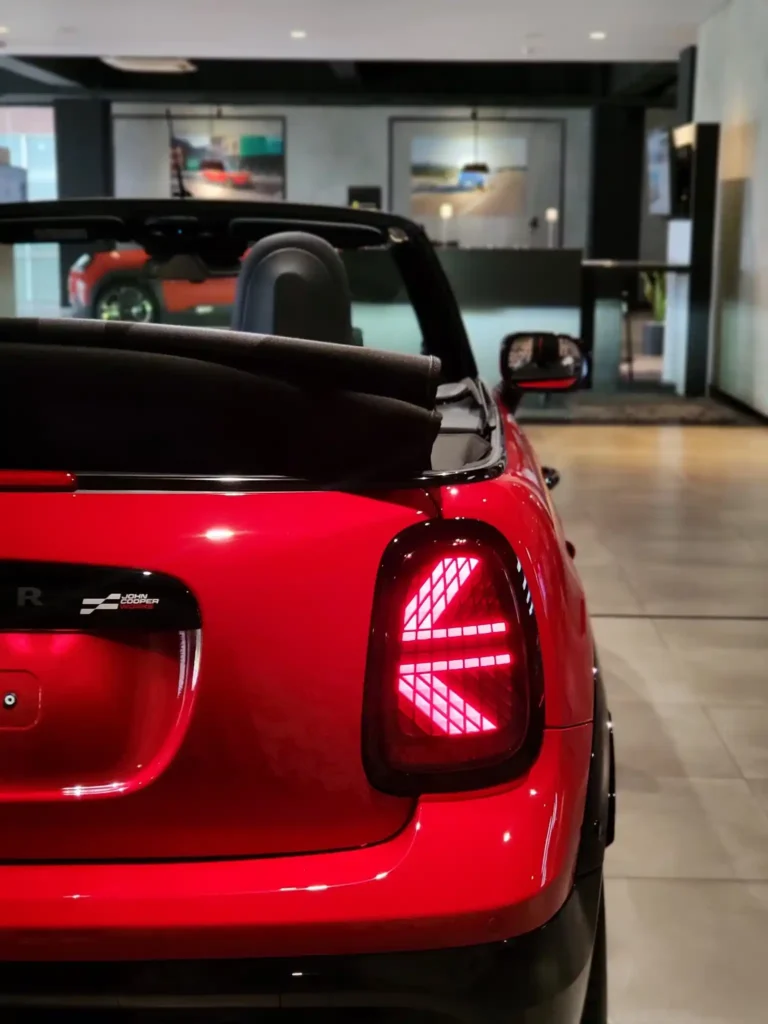 Tampak belakang Mini Cooper bekas merah dengan lampu Union Jack menyala di dalam showroom modern.