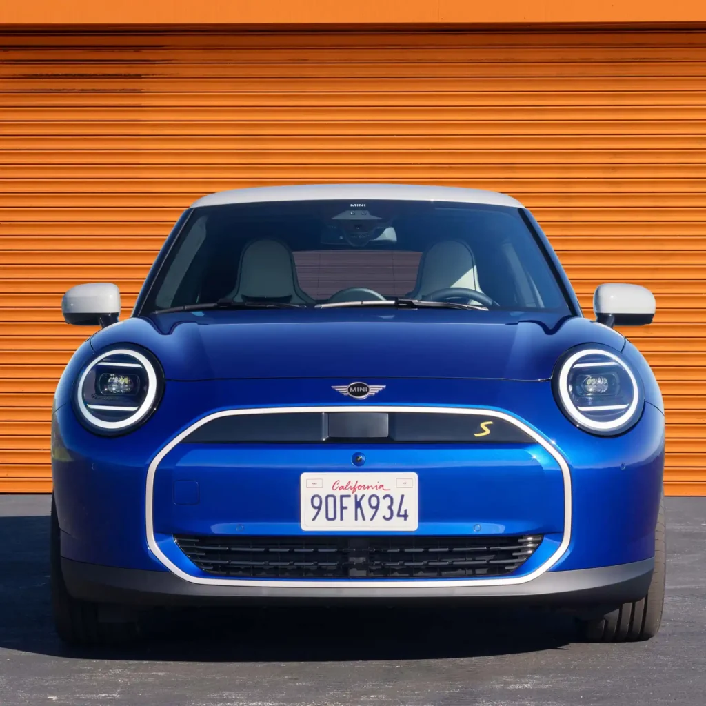 MINI 3 DOOR ELECTRIC, Tampak depan mini cooper se 2024 warna biru di depan latar oranye